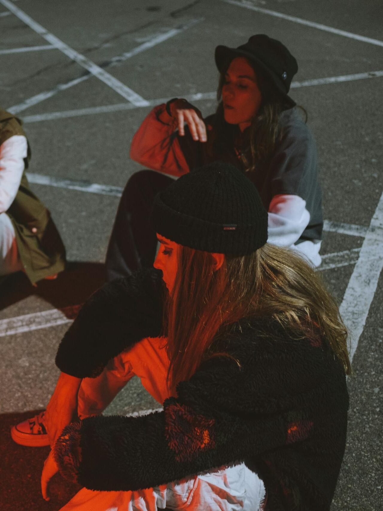 Three young women sitting and relaxing in a parking lot under dramatic lighting.